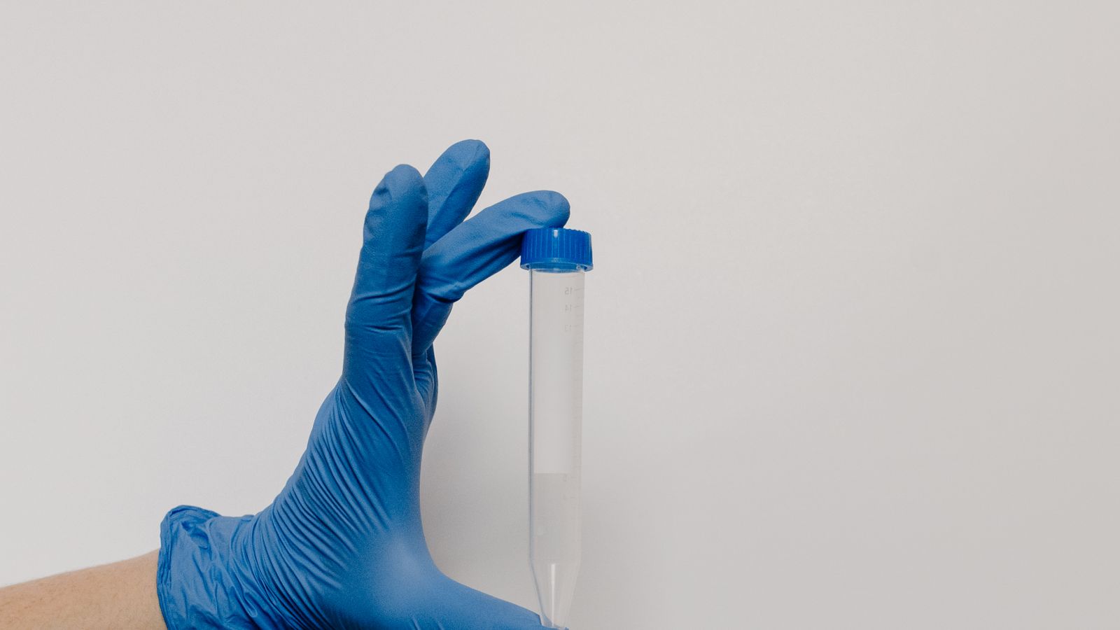 A blue-gloved hand holds a transparent test tube against a white background.
