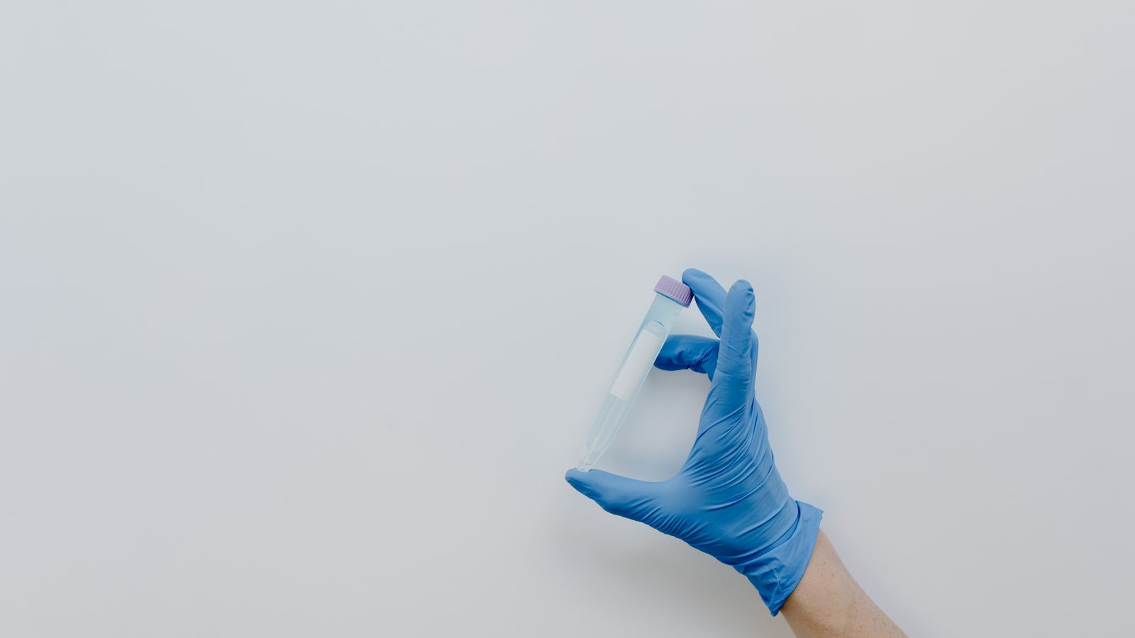A gloved hand holds a small centrifuge tube against a plain, neutral background.