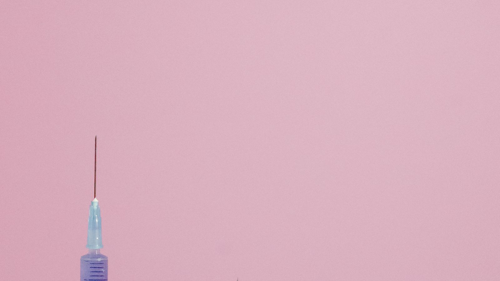 Three syringes of different sizes standing upright against a soft pastel pink backdrop.